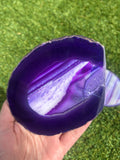 Purple agate stone held in a hand with grass in the background