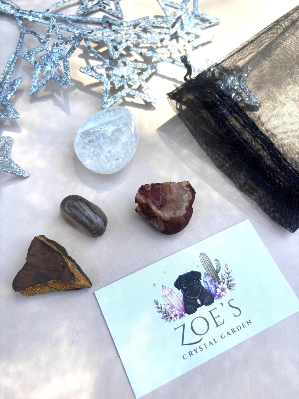 Mineral specimens and a clear crystal on a white surface with 'Zoe's Crystal Garden' branding.