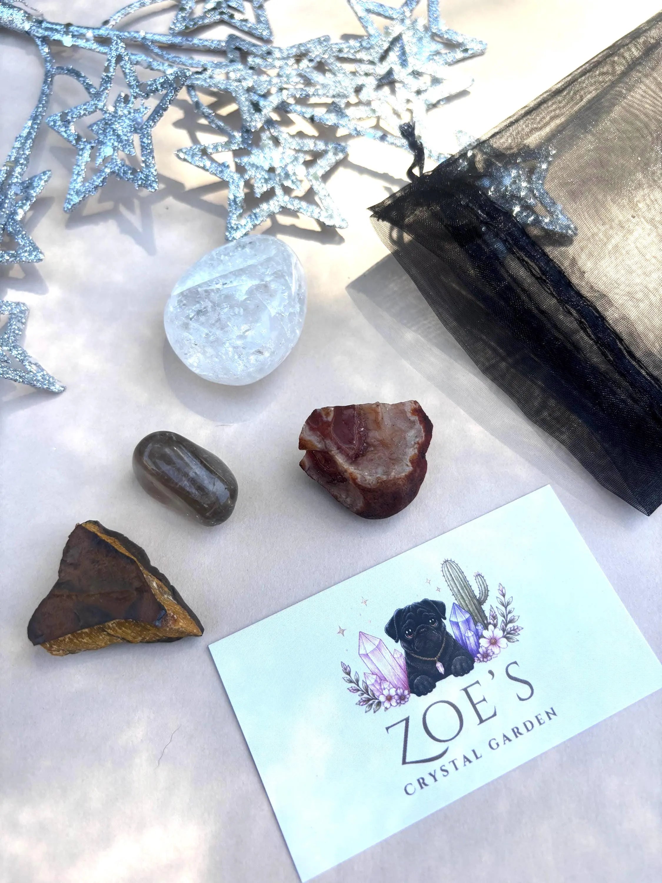 Mineral specimens and a clear crystal on a white surface with 'Zoe's Crystal Garden' branding.